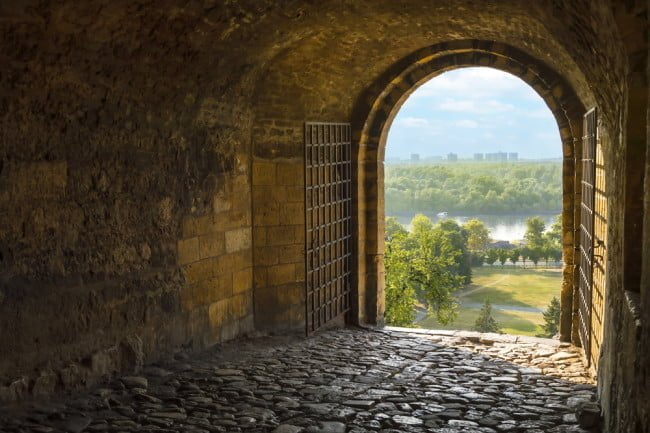 looking out of a dark castle gate into wide open landscape
