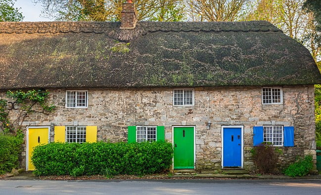 Row of thatched cottages with doors painted in different colours.