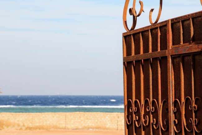 rusty gate opening to view of beach and sea